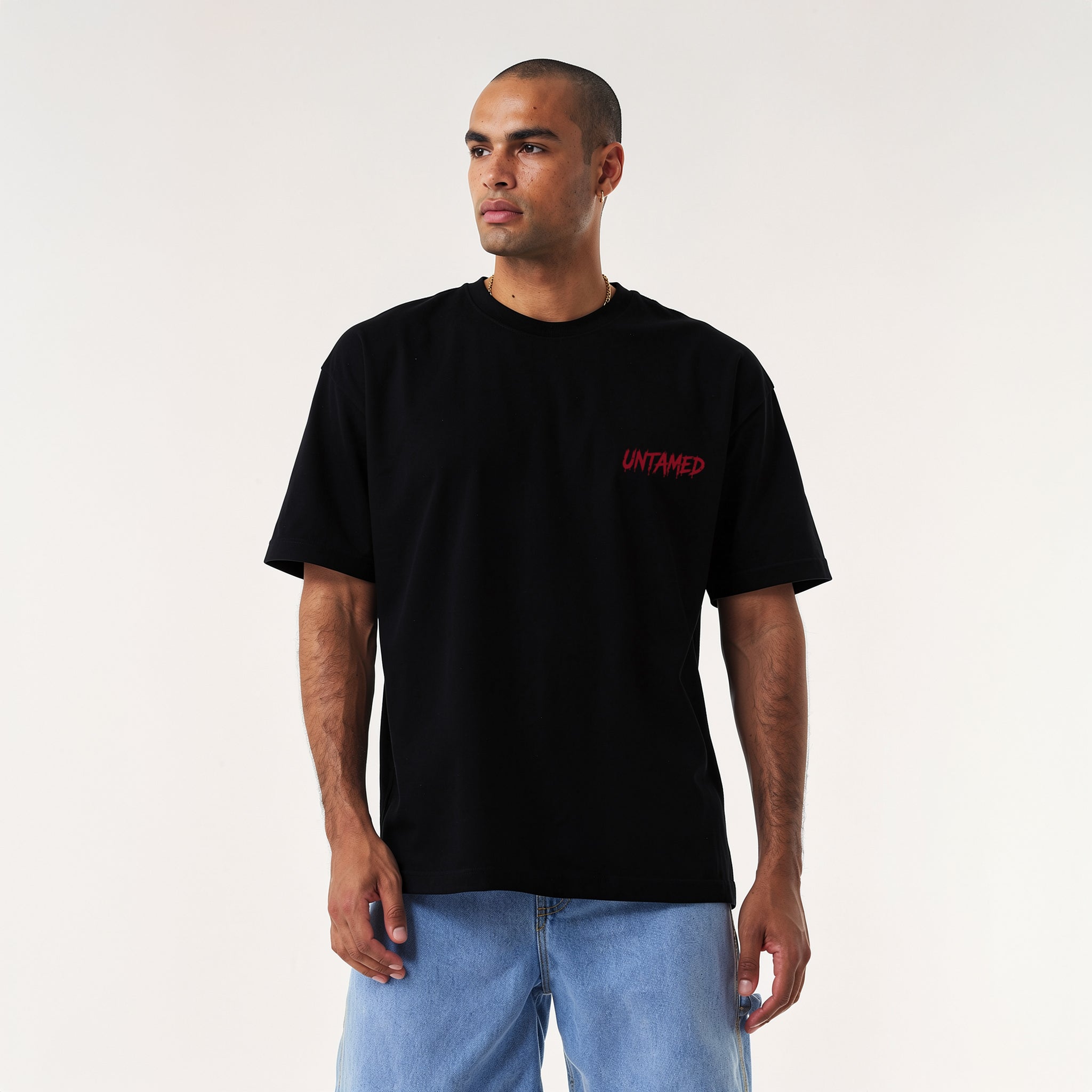 oversized streetwear t-shirt. Front shows the word UNTAMED in red dripping text. Back features an aggressive Doberman dog with a spiked collar, chains, bones, and a red triangle background.