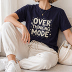 White hand-drawn typography saying Overthinking Mode with laptop and book doodles on a dark premium t-shirt.